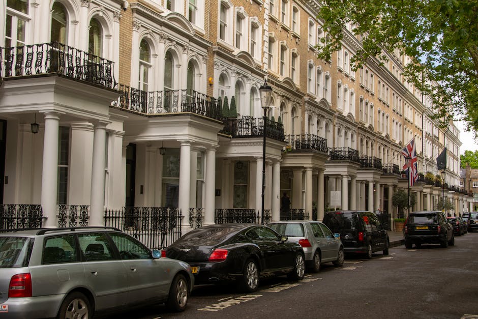 Photograph of a residential street featuring a white, Victorian-style house with ornate architectural details, including decorative cornices, arched windows, and a small balcony with a wrought iron ra