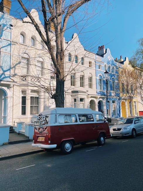 A street scene in Pimlico showing a row of multi-storey residential buildings with classic architectural details and large windows, set against a blue sky with some clouds. The pavement is lined with